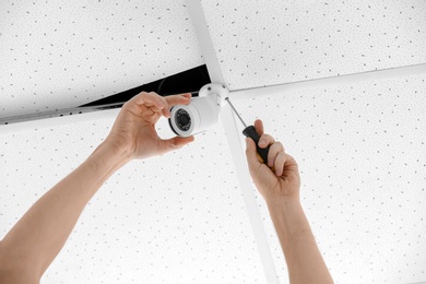 Photo of Technician installing CCTV camera on ceiling indoors