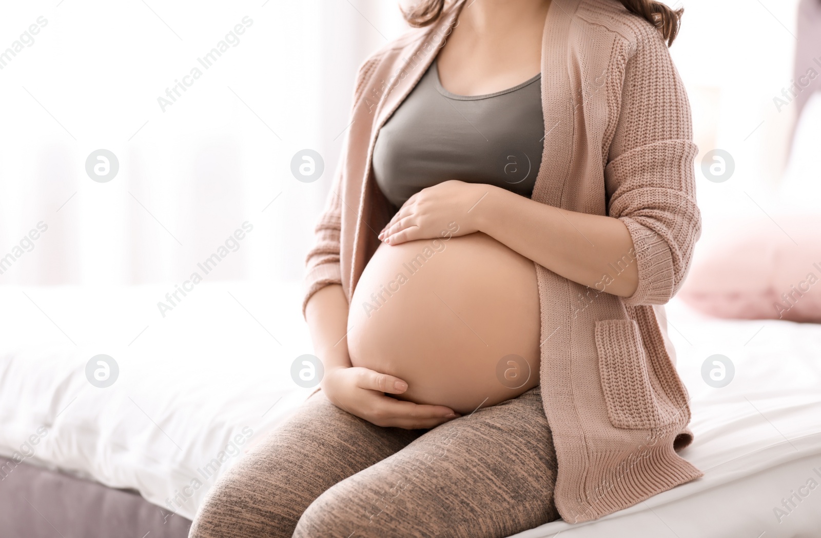 Photo of Young pregnant woman sitting on bed at home