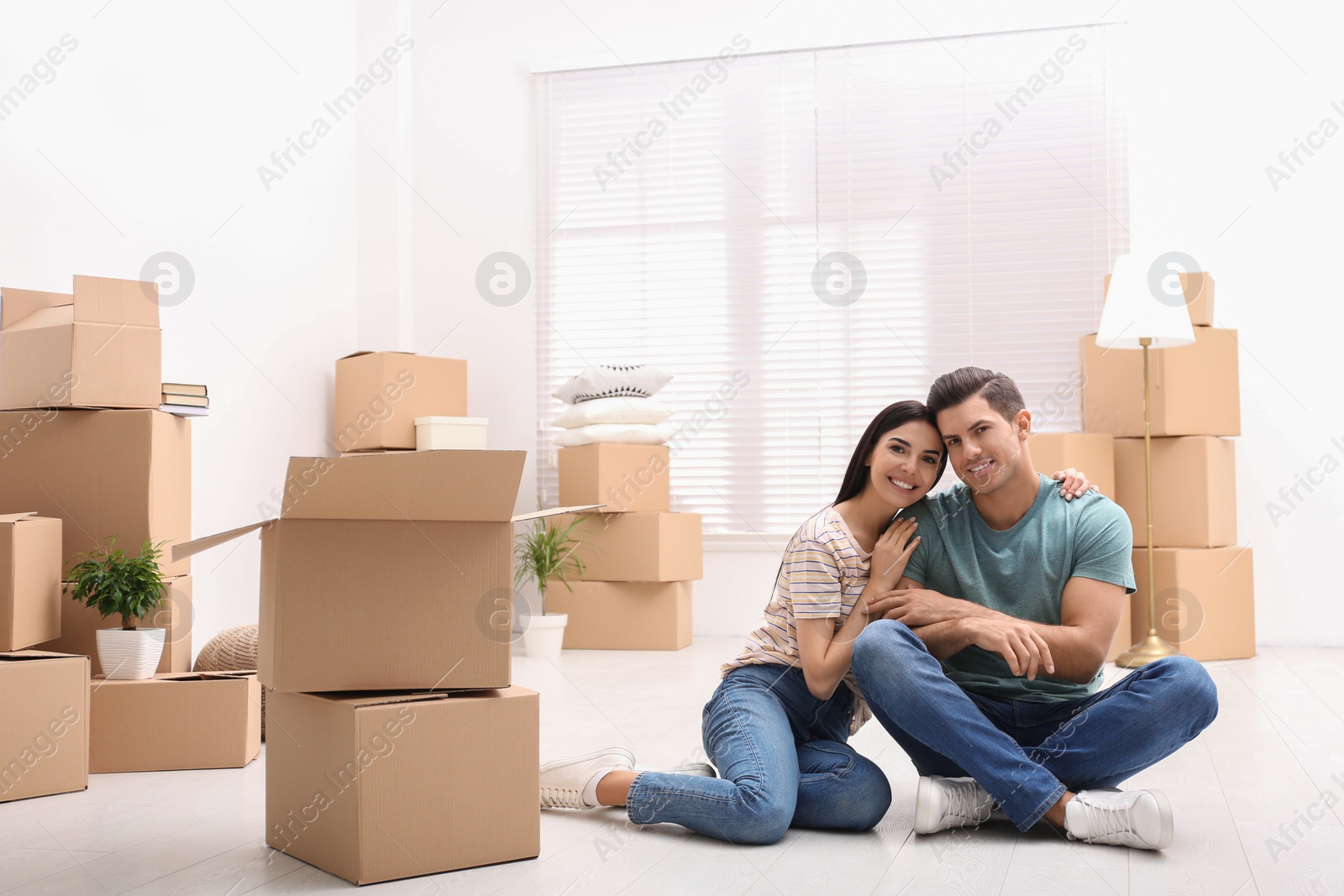 Photo of Happy couple in room with cardboard boxes on moving day