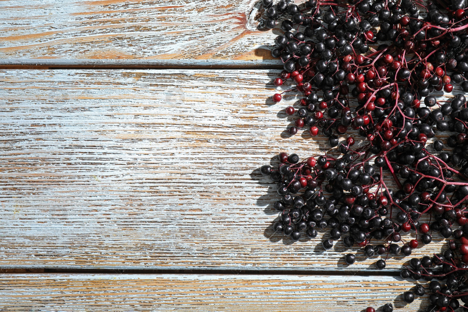 Photo of Black elderberries (Sambucus) on old wooden table, flat lay. Space for text