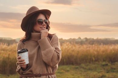 Photo of Beautiful young woman with cup of coffee wearing stylish autumn sweater outdoors