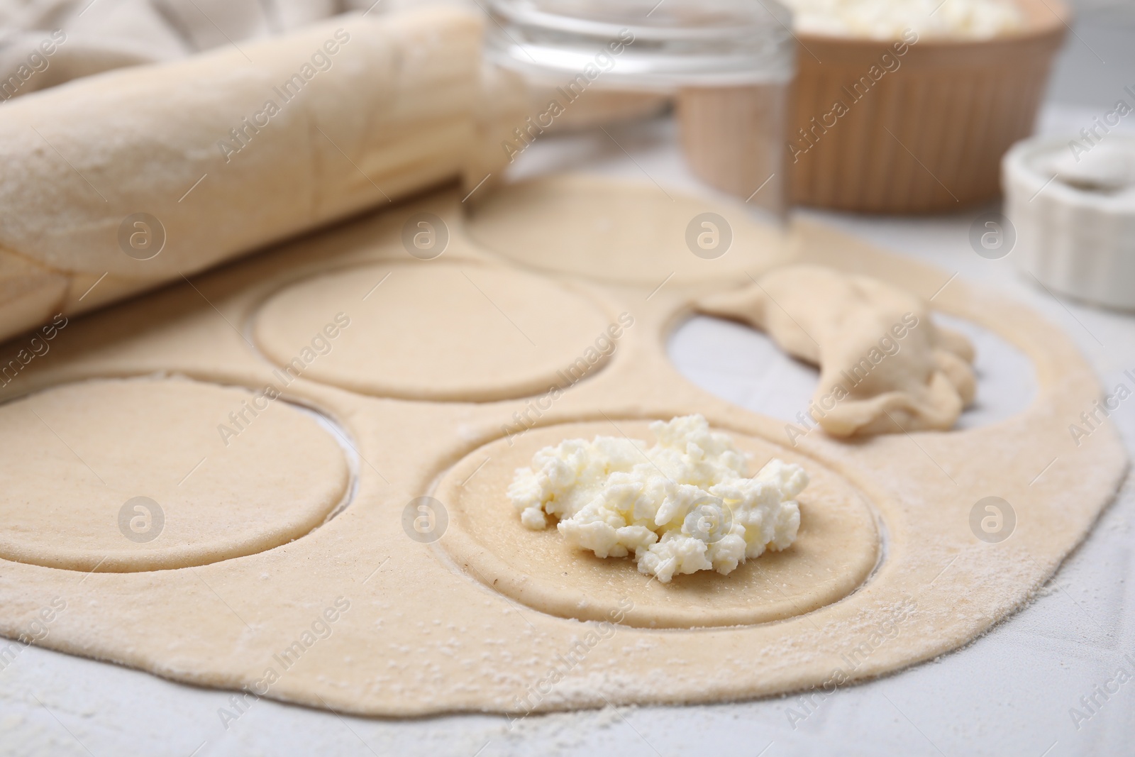 Photo of Process of making dumplings (varenyky) with cottage cheese. Raw dough and ingredients on white table, closeup