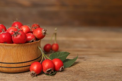 Photo of Ripe rose hip berries with green leaves on wooden table, closeup. Space for text