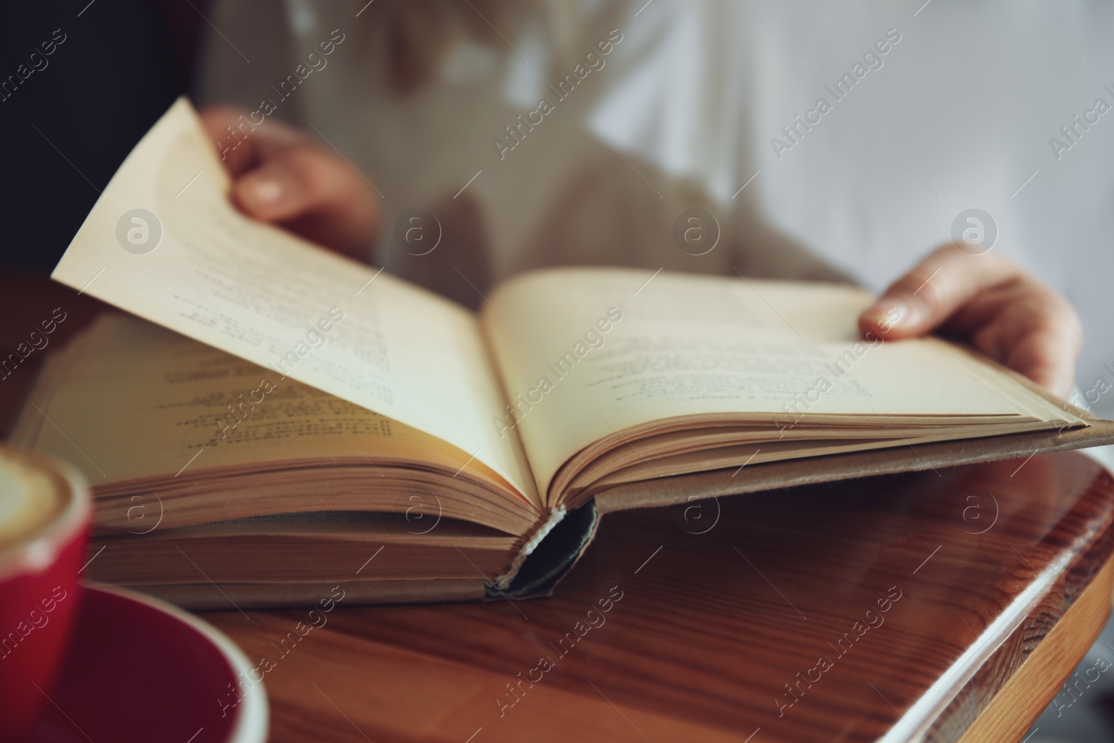 Photo of Woman reading book at table indoors, closeup