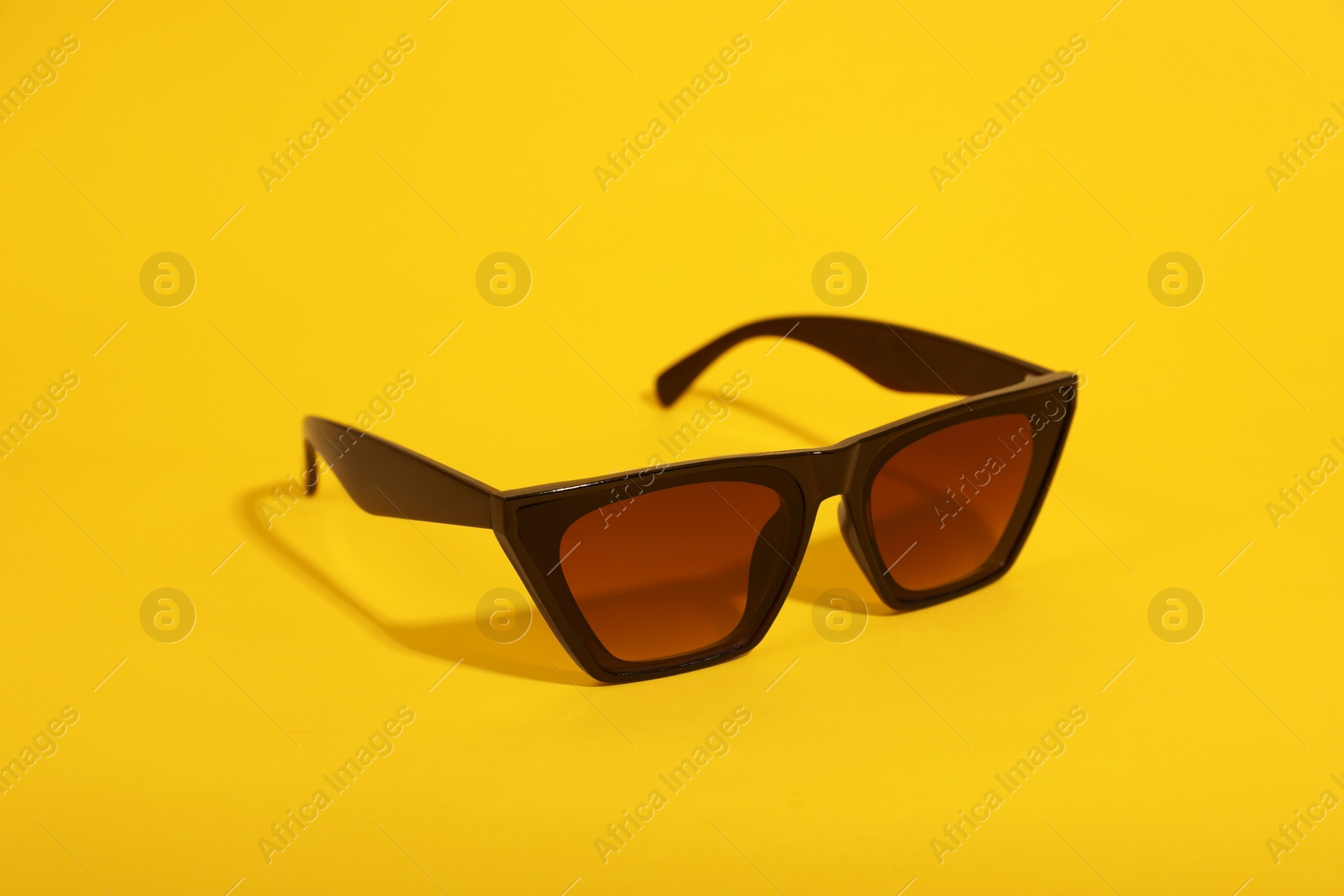 Photo of Stylish sunglasses with black frame on yellow background