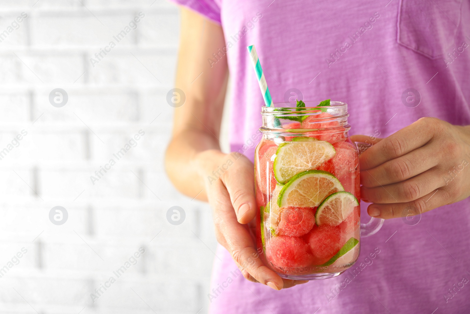 Photo of Young woman with tasty refreshing watermelon drink near light wall, closeup