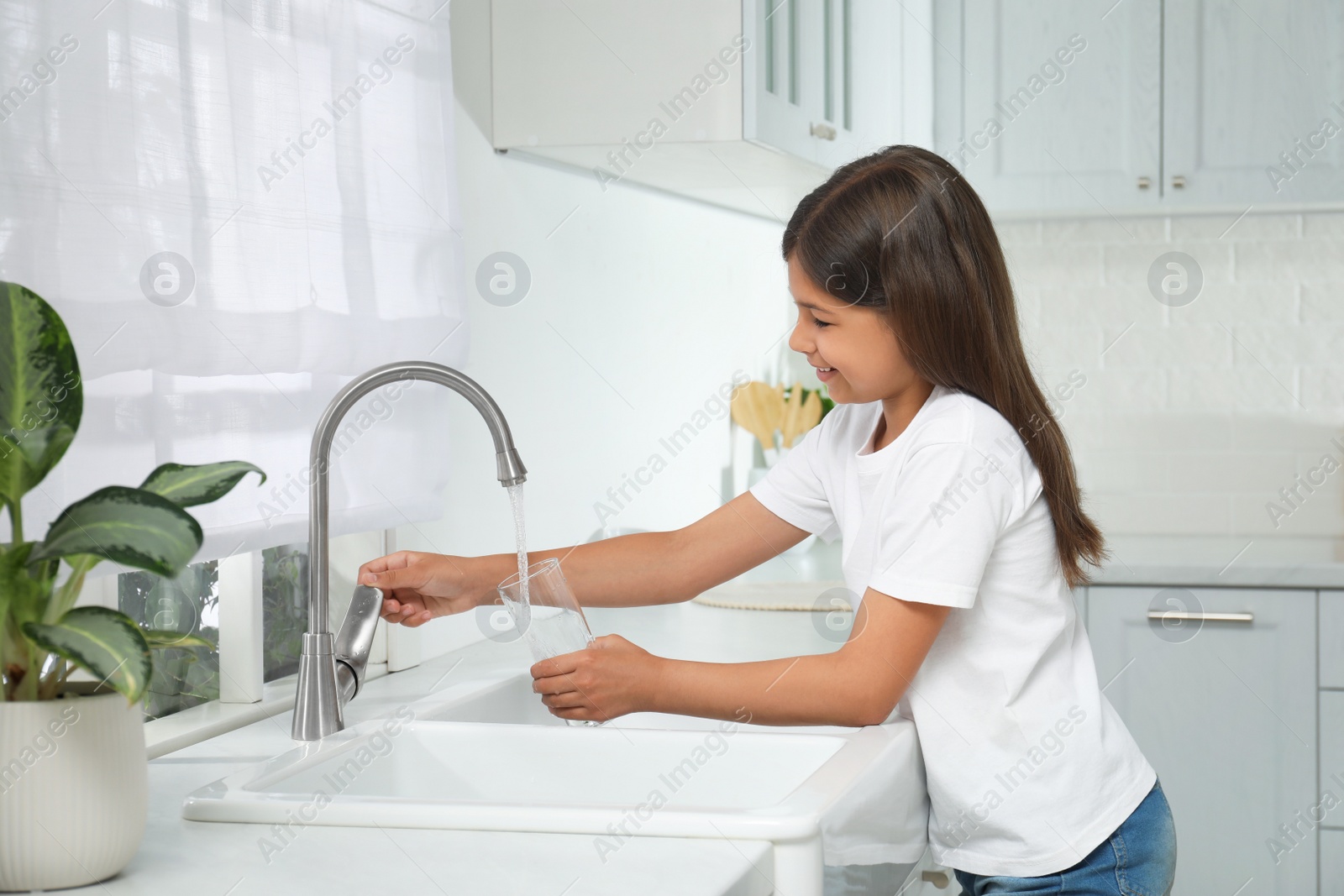 Photo of Girl filling glass with water from tap in kitchen