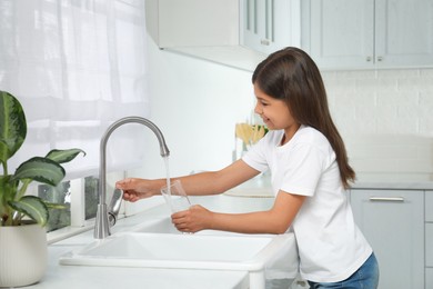 Photo of Girl filling glass with water from tap in kitchen