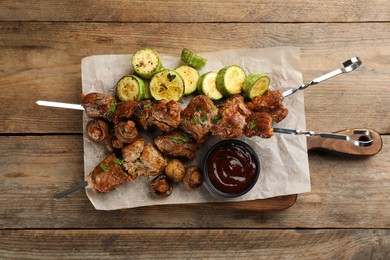 Metal skewers with delicious meat, ketchup and vegetables on wooden table, top view