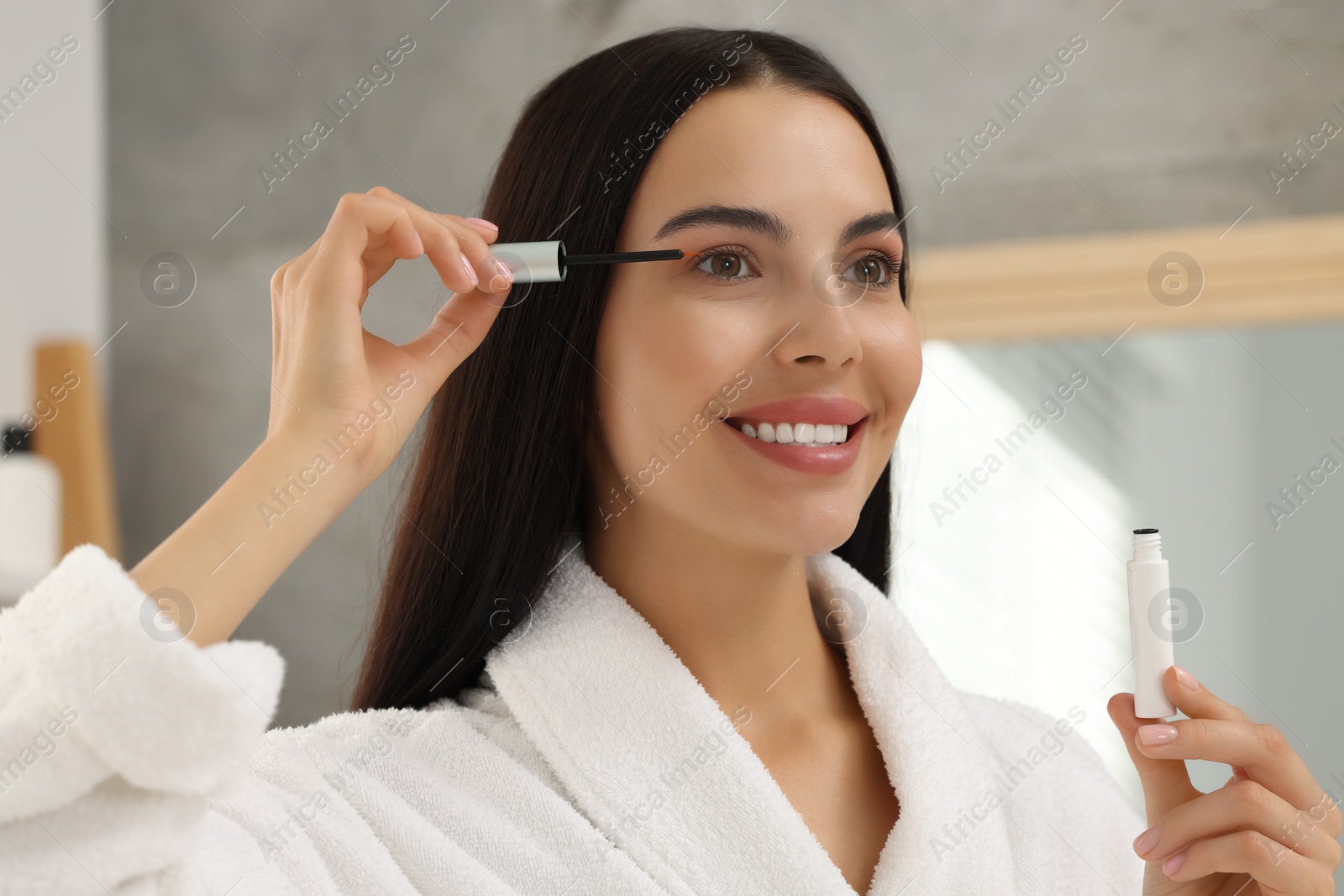 Photo of Beautiful woman applying serum onto her eyelashes indoors. Cosmetic product