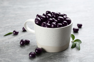 Fresh acai berries in mug on light grey table, closeup