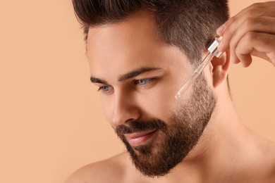 Photo of Handsome man applying cosmetic serum onto face on beige background, closeup