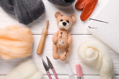 Felted bear, wool and tools on white wooden table, flat lay