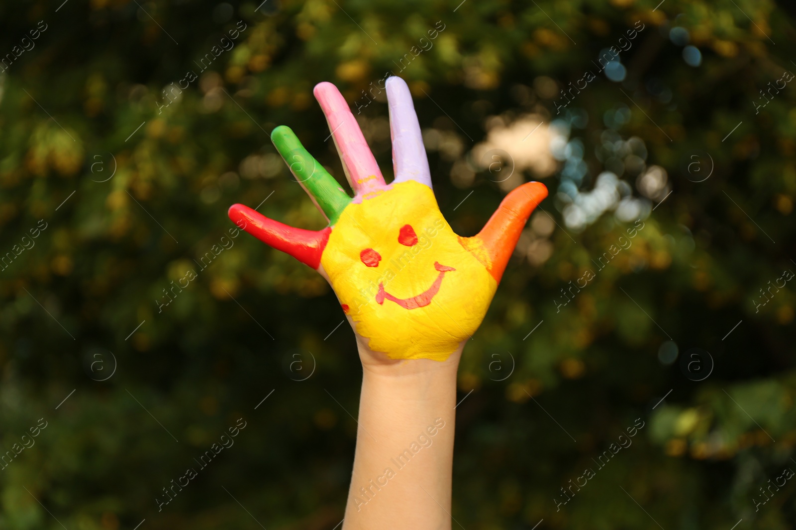 Photo of Kid with smiling face drawn on palm in green park, closeup. School holidays