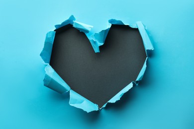 Photo of Torn heart shaped hole in light blue paper on black background