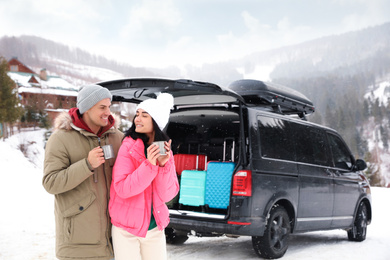 Happy couple with drinks near car on snowy road. Winter vacation