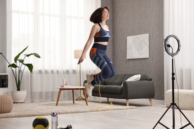 Photo of Happy sports blogger jumping with rope while streaming online fitness lesson with smartphone at home