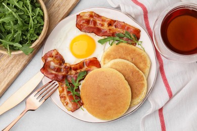 Photo of Tasty pancakes with fried egg, arugula and bacon served on light grey table, flat lay
