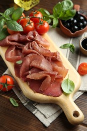 Photo of Board with delicious bresaola served with other snacks on wooden table