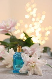 Photo of Bottle of perfume and beautiful lily flowers on table against beige background with blurred lights, closeup