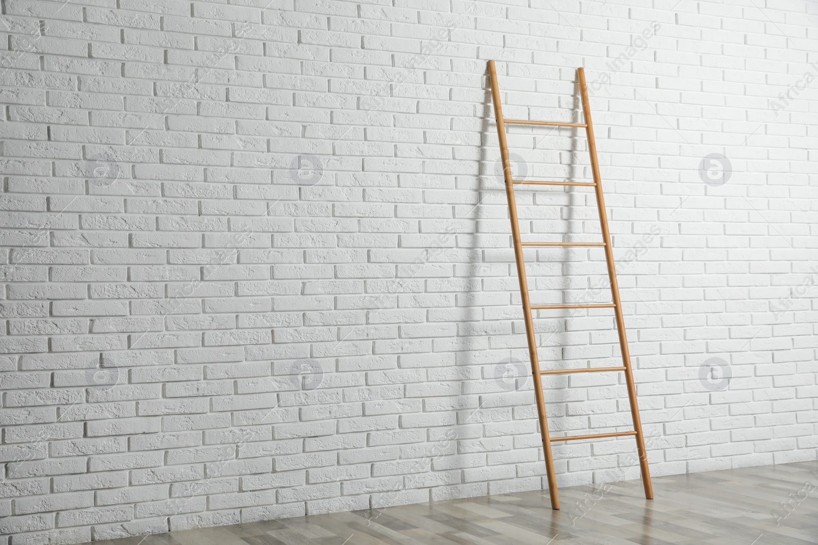 Photo of Modern wooden ladder near white brick wall. Space for text