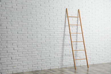 Modern wooden ladder near white brick wall. Space for text