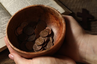 Donate and give concept. Woman holding bowl of coins at table, closeup