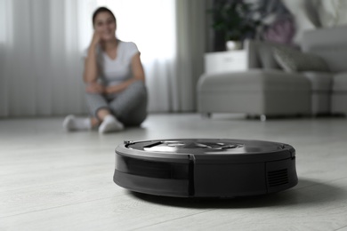 Photo of Modern robotic vacuum cleaner and blurred woman on background