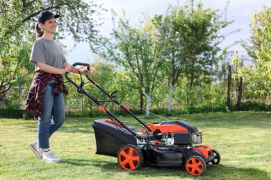 Photo of Smiling woman cutting green grass with lawn mower in garden