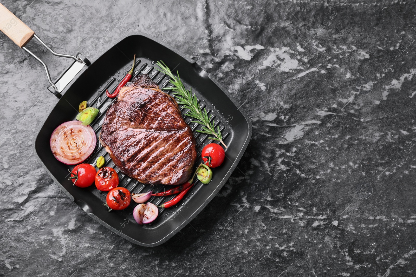 Photo of Grill pan with delicious fried beef meat, spices and vegetables on grey textured table, top view. Space for text