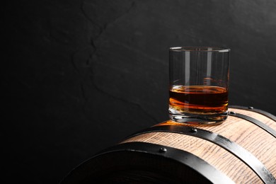 Photo of Glass of whiskey on wooden barrel against grey background, space for text
