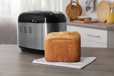 Photo of Breadmaker and fresh homemade bread on wooden table in kitchen