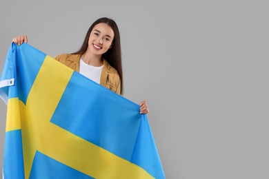Photo of Young woman holding flag of Sweden on light grey background, space for text