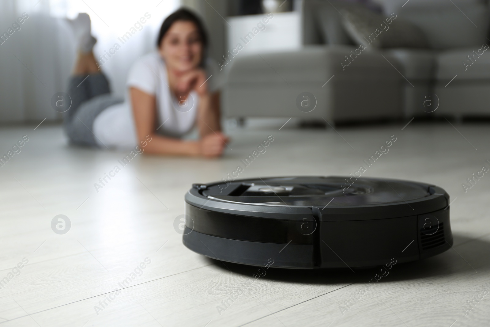 Photo of Modern robotic vacuum cleaner and blurred woman on background