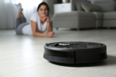 Photo of Modern robotic vacuum cleaner and blurred woman on background