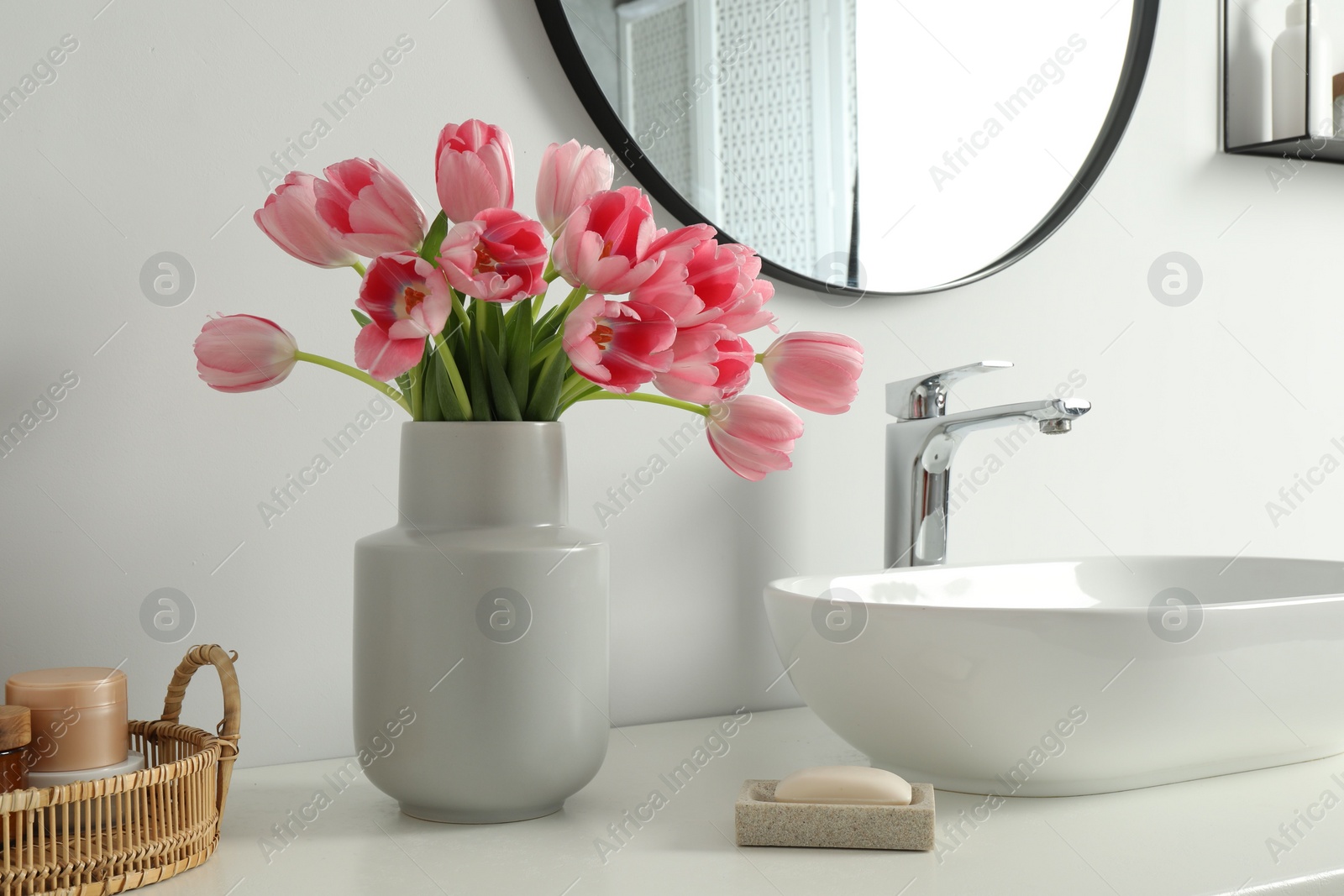 Photo of Vase with beautiful pink tulips and toiletries near sink in bathroom