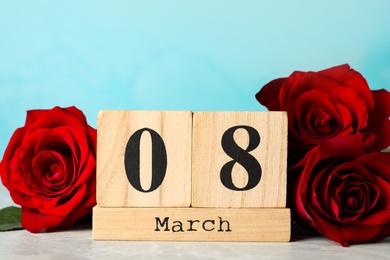 Photo of Wooden block calendar with date 8th of March and roses on table against light blue background. International Women's Day