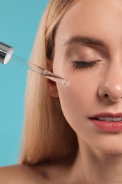 Photo of Beautiful woman applying cosmetic serum onto her face on light blue background, closeup