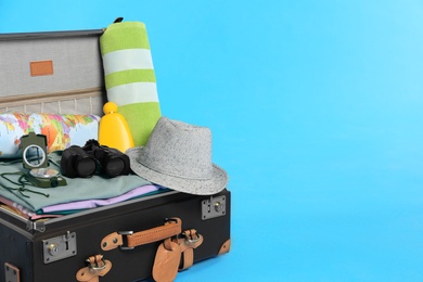 Photo of Packed vintage suitcase with clothes on light blue background, space for text. Summer vacation