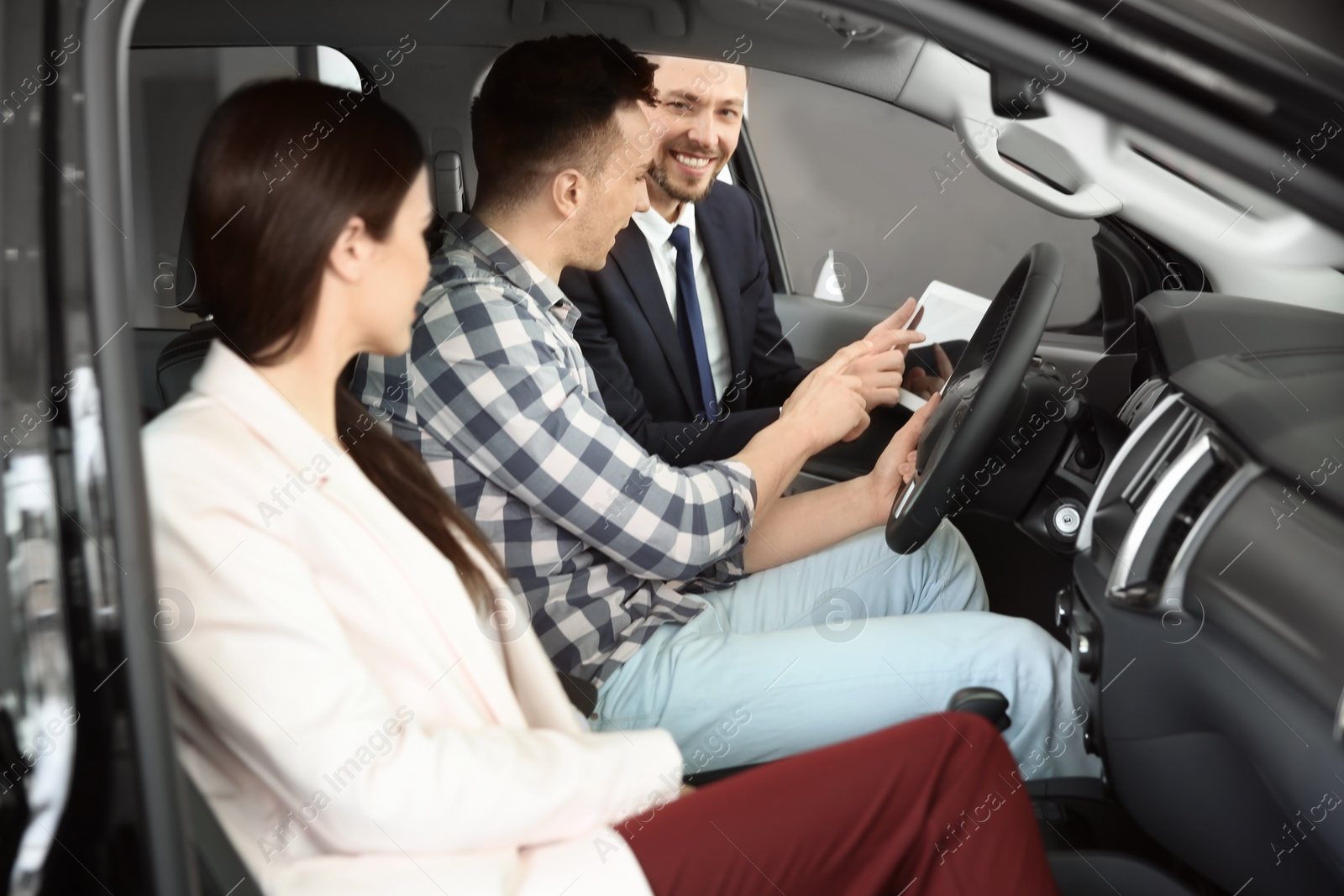 Photo of Salesman consulting young couple in auto at dealership. Buying new car