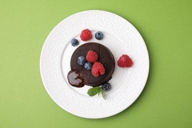 Plate with delicious chocolate fondant, berries and mint on light green table, top view