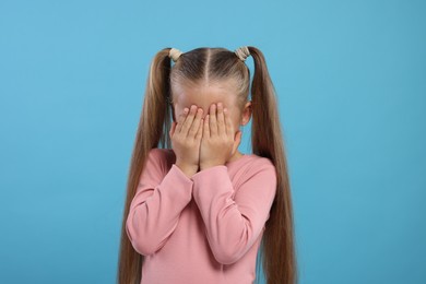 Resentful girl covering her face with hands on light blue background