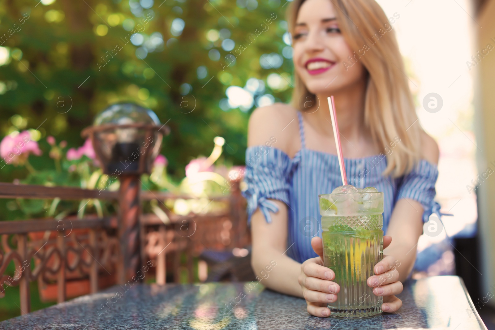 Photo of Young woman with glass of tasty lemonade at table in cafe, outdoors. Natural detox drink