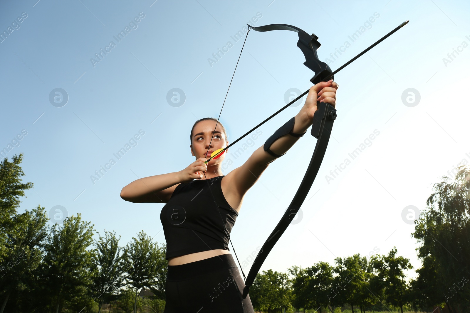 Photo of Woman with bow and arrow practicing archery outdoors, low angle view