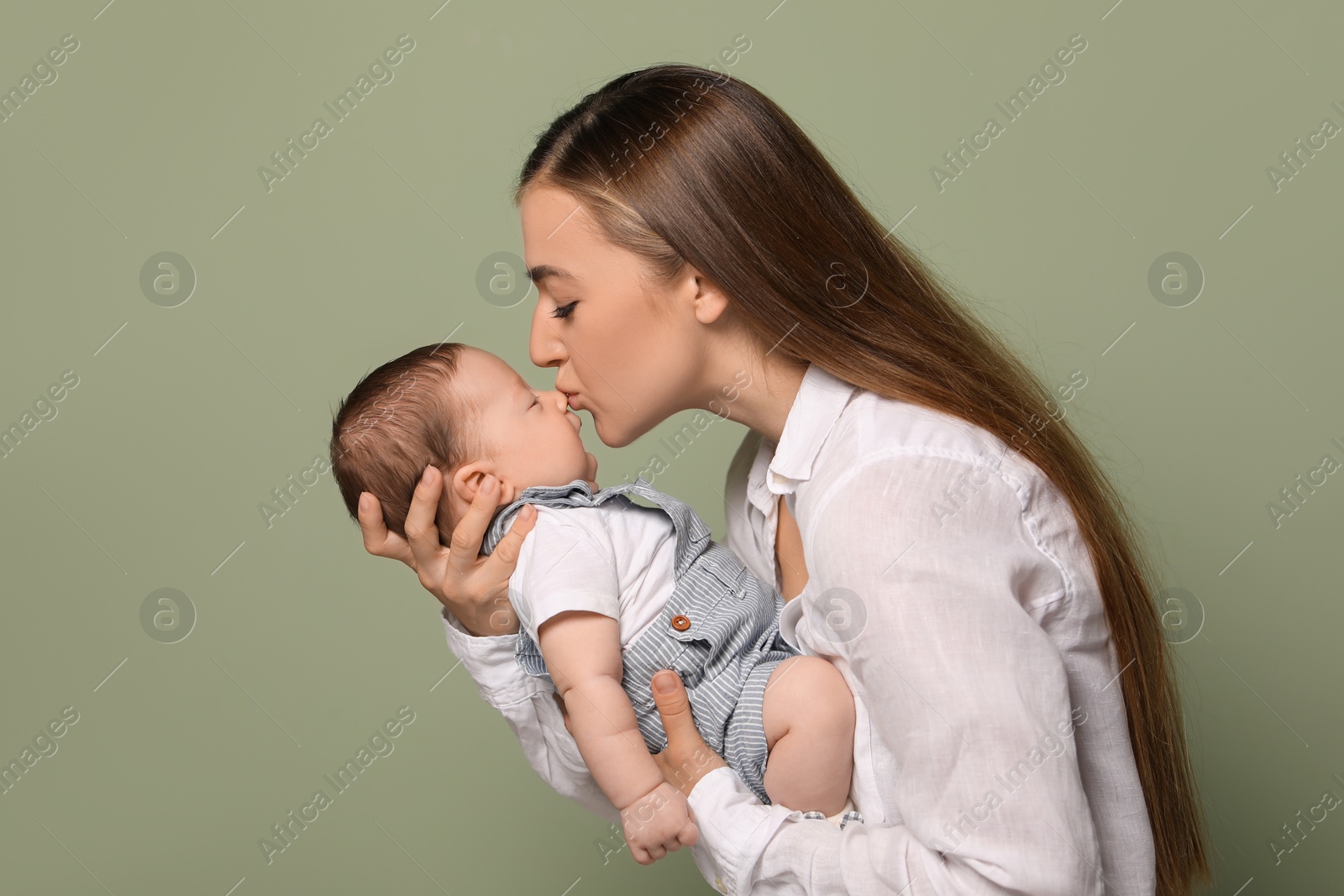 Photo of Mother kissing her cute newborn baby on olive background