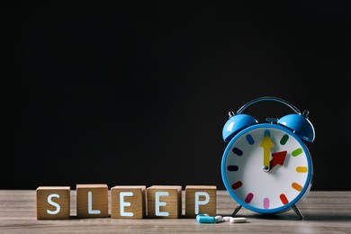 Word Sleep made with cubes, alarm clock and pills on wooden table, space for text. Insomnia treatment