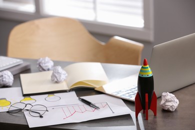 Photo of Toy rocket, laptop and stationery on messy table in office, space for text. Startup concept