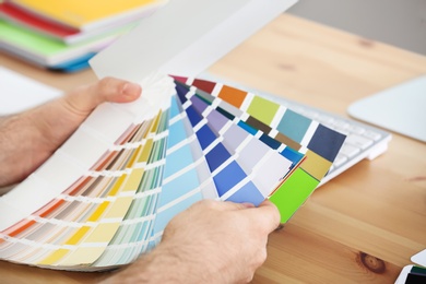 Photo of Designer with paint color palette samples at table, closeup