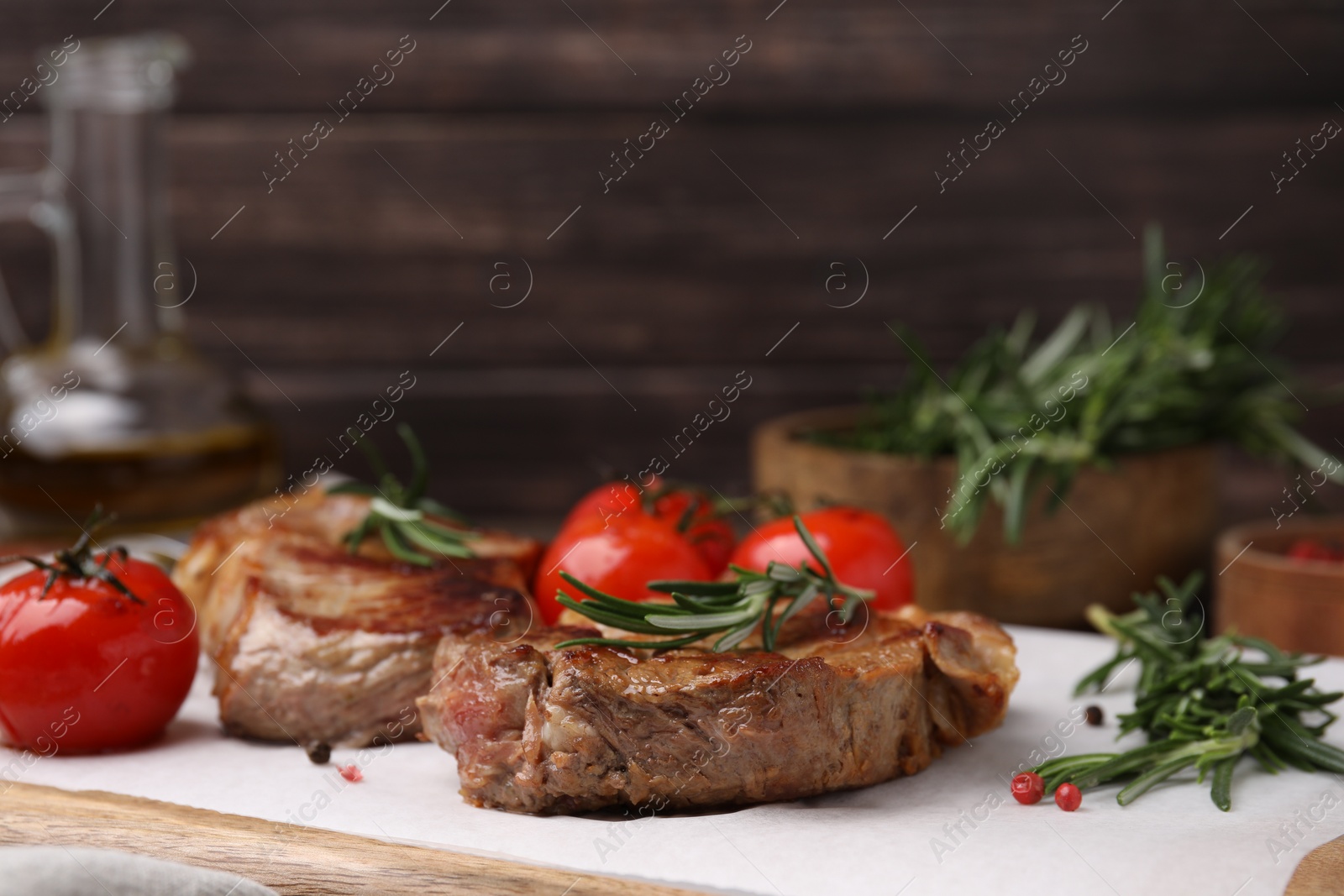 Photo of Delicious fried meat with rosemary and tomatoes on wooden board, closeup