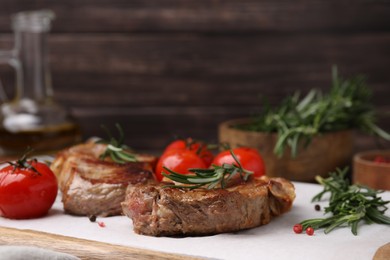 Delicious fried meat with rosemary and tomatoes on wooden board, closeup